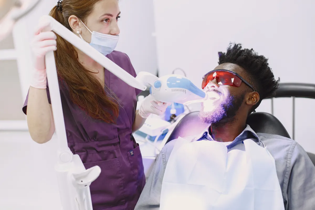 Dental clinician using a whitening light during supervised in-clinic teeth whitening.